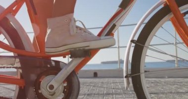 Deniz kenarında güneşli bir günde genç bir beyaz adama doğru bisiklet süren beyaz bir kadının alçak kesimi, ağır çekim.