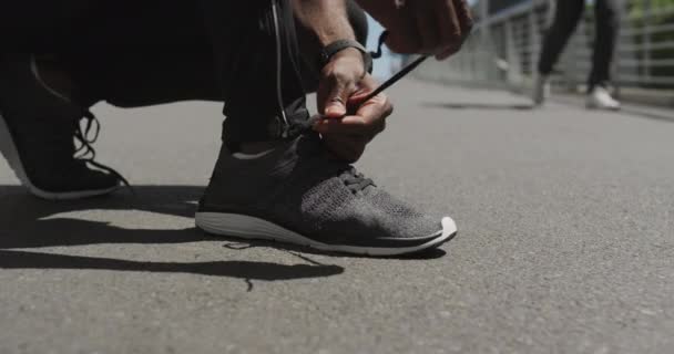 市内で晴れた日に訓練する前に 彼の靴を結ぶ通りにひざまずいてスポーツ服を着てアフリカ系アメリカ人の男性の低セクションのビュー スローモーション — ストック動画
