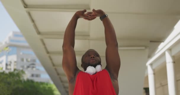 市内の晴れた日に訓練しながら 橋の下にストレッチ空気中の彼の腕でスポーツウェアで運動アフリカ系アメリカ人の男性のフロントビュー スローモーション — ストック動画