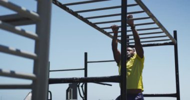 Spor kıyafetleri içinde, güneşli bir günde şehir parkındaki bir spor salonunda maymunla egzersiz yapan kulaklık takan Afro-Amerikan bir adamın ön görüntüsü.