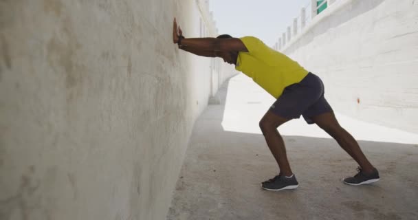 スポーツウェアを着たアフリカ系アメリカ人の男性の側面図は 市内の晴れた日に地下道の壁に向かって押すと スローモーション — ストック動画
