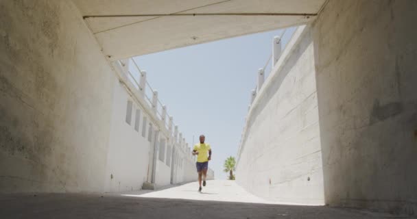 市内の晴れた日に地下を走るスポーツウェアを着たアフリカ系アメリカ人の男性のフロントビュー スローモーション — ストック動画