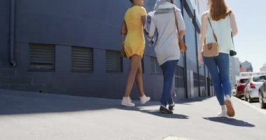 Kafkasyalı genç bir kadın, genç bir Afrikalı Amerikalı kadın ve tesettürlü genç bir ırk kadını güneşli bir caddede yürürken ve konuşurken kahve içerken, ağır çekimde