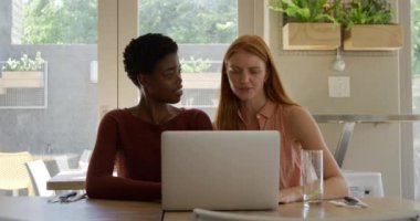 Kafkasyalı, uzun kızıl saçlı genç bir kadın ve bir kafede oturan, konuşan ve dizüstü bilgisayara bakan genç bir Afro-Amerikan kadın. Ağır çekim.