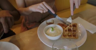 Genç bir Afro-Amerikalı ve Kafkasyalı bir kadının orta kesiminde bir kafede oturmuş waffle yiyor.