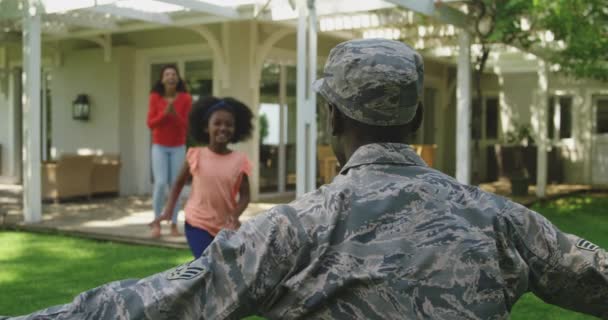 若い娘は彼を迎えるために実行しながら 彼の家の外の庭にひざまずいて若い大人のアフリカ系アメリカ人男性兵士の後部ビューと彼の混合レース妻は彼女の後ろを歩く スローモーション — ストック動画