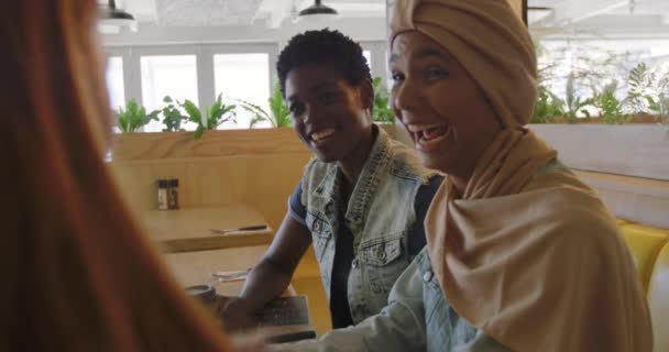 若いアフリカ系アメリカ人の女性とヒジャーブを着た若い人種の女性がコーヒーショップに座って話をしたり笑ったりゆっくりとした動きをしていました — ストック動画