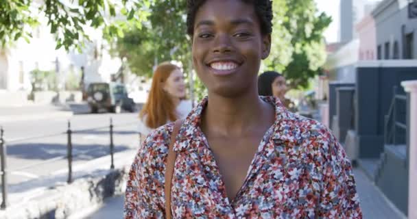 若いアフリカ系アメリカ人女性がカメラに笑顔で街を歩いている姿を描いた彼女の2人の女性の友人が彼女の後ろを歩いている — ストック動画