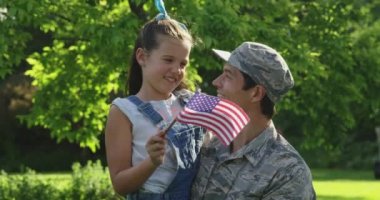 Genç bir yetişkinin portresi evinin bahçesinde, elinde Amerikan bayrağı sallayan ve kameraya gülümseyen kızını taşıyan melez bir erkek askerin fotoğrafı.