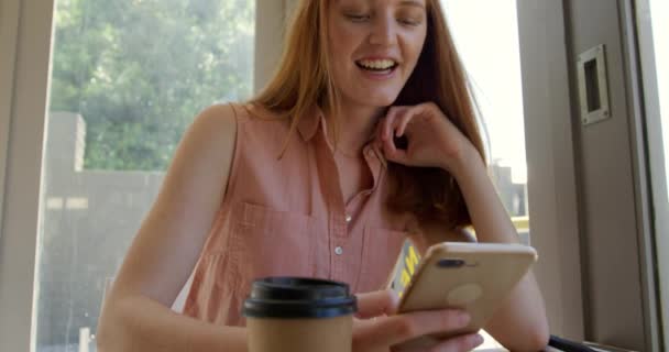 一位快乐的白种人年轻女子 一头长长的红头发 坐在咖啡店里 她用智能手机 动作缓慢 她的前景非常逼真 — 图库视频影像