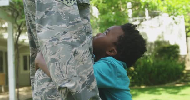 彼の家の外の庭に若い大人のアフリカ系アメリカ人男性兵士の側のビューのセクションでは 彼を見ている彼の若い息子を受け入れ 笑顔と私たちのフラグを保持し 背景に彼らの家 スローモーション — ストック動画