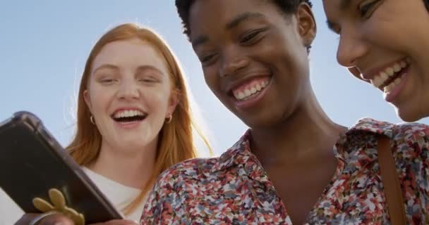 若い白人女性 若いアフリカ系アメリカ人女性 ヒジャーブを身に着けている若い混合人種の女性のフロントビュー一緒にスマートフォンを見て 太陽の光に照らされ スローモーション — ストック動画