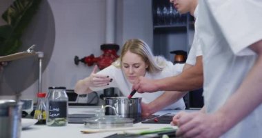 Profesyonel Kafkasyalı kadın şef bir restoranda beyaz şefler giyiyor, yemek hazırlıyor ve meslektaşları ağır çekimde ön planda çalışıyor.