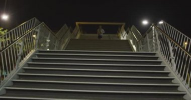 Beyaz giyimli bir adamın düşük açılı görüntüsü, gece boyunca şehir sokaklarında egzersiz yapması, antrenman sırasında aşağıya koşması..