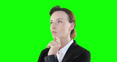 Düşünceli, çekici, kahverengi saçlı, şık kıyafetler giyen, yeşil arka planda merak ederken gülümseyen ve yüzüne dokunan beyaz kadın..