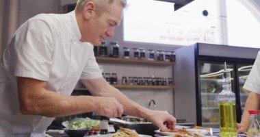 Kafkasyalı profesyonel bir aşçı lokanta mutfağında aşçı beyazı giyer ve ağır çekimde yemek hazırlar.