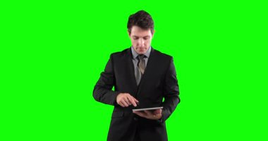 Beyaz iş adamı, kısa siyah saçlı, açık renk gömlekli, koyu renk ceketli, tabletini yeşil ekran arka planında tutuyor ve kullanıyor.