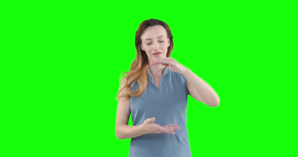 快乐迷人的白种人女人 一头棕色长发 穿着一件聪明的灰色衬衫 前臂高举 在绿色背景上呈现出虚拟的互动画面 — 图库视频影像
