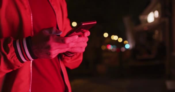 一个身穿休闲装的白人男子的中间部分 晚上在城市街道上边走边用智能手机 — 图库视频影像