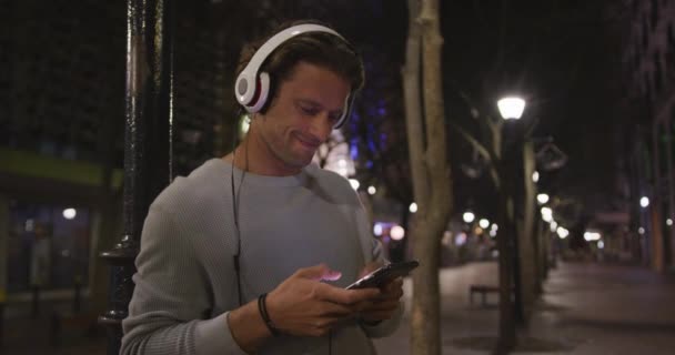 Běloch Šedém Svetru Noci Venku Ulicích Města Používá Smartphone Sluchátka — Stock video