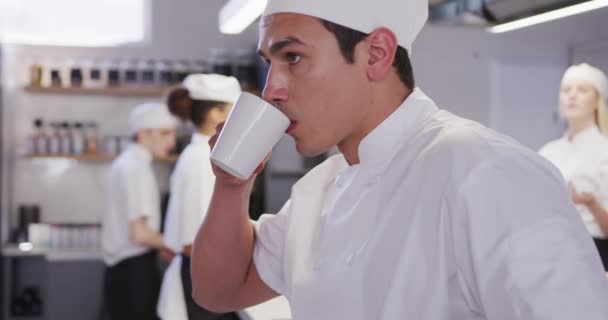전문적 주방장은 주방에서 요리사들을 고용하고 머그잔을 마시며 동료들 뒷자리에서 동작으로 — 비디오