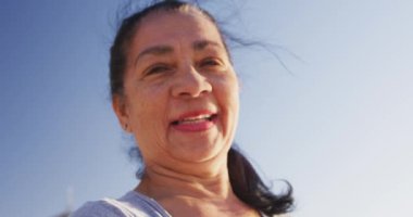 Güneşli bir günde kumsalda egzersiz yapmaktan zevk alan, yoga yapan, kameraya bakan beyaz bir kadının portresi.