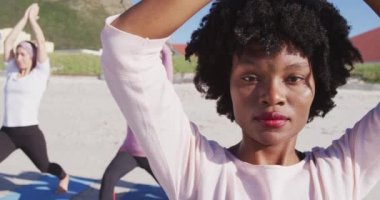 Çok ırklı bir grup kız arkadaş güneşli bir günde kumsalda egzersiz yapıyor yoga yapıyor, yoga pozisyonunda geriniyor..