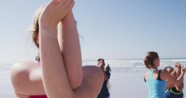 Çok ırklı bir grup kız arkadaş güneşli bir günde kumsalda egzersiz yapıyor yoga yapıyor, yoga pozisyonunda geriniyor..