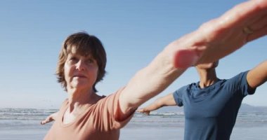 Çok ırklı bir grup kız arkadaş güneşli bir günde kumsalda egzersiz yapıyor yoga yapıyor, yoga pozisyonunda geriniyor..