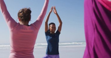 Çok ırklı bir grup kız arkadaş güneşli bir günde kumsalda egzersiz yapıyor yoga yapıyor, yoga pozisyonunda geriniyor..
