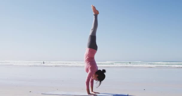 在阳光充足的海滩上 身穿运动服 练习瑜伽 双手高举瑜伽姿势的混合泳美女 — 图库视频影像