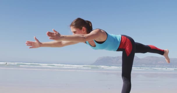 白人美女 穿着运动服 练瑜伽 站在瑜伽位置上 在阳光灿烂的海滩上 — 图库视频影像