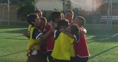 Güneşli bir günde, yeşil bir futbol sahasında futbol oynayan iki çocuk takımından oluşan çok ırklı bir grup bir hedefi kutluyor, sarılıyor ve zıplıyorlar.