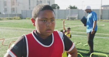 Güneşli bir günde sahada durup antrenman sırasında dinlenen ve arka planda takım arkadaşları olan Afrikalı Amerikalı bir futbolcunun portresi.