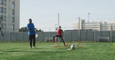 Çok ırklı erkek futbol oyuncularından oluşan bir grup antrenörleriyle güneşin altında bir oyun alanında antrenman yapıyor.