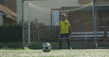 Takım elbiselerini giyen çok ırklı erkek futbol oyuncularından oluşan bir grup, bir futbol sahasında maç yaparken, bir çocuk golü atıyor.