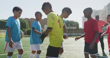 Yeşil bir futbol sahasındaki futbol maçından önce, güneşli bir günde iki sıra halinde duran, el sıkışan iki çocuk takımından oluşan çok ırklı bir grup.