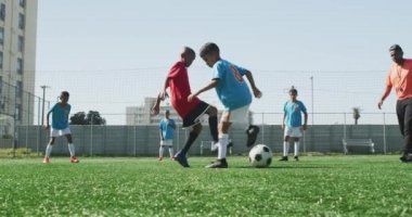 Güneşli bir günde, yeşil bir futbol sahasında futbol oynayan iki çocuk takımından oluşan çok ırklı bir grup.