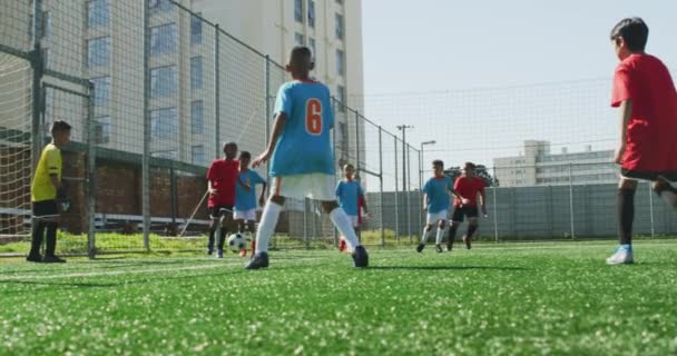 在一个阳光明媚的日子里 由两个孩子组成的多民族团体在一个绿色的足球场上踢足球 经过并射击 — 图库视频影像