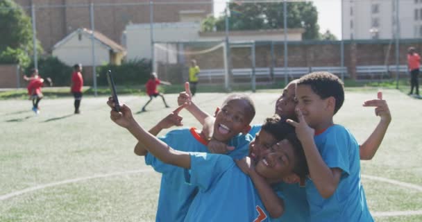 在一个阳光灿烂的日子里 由两个孩子组成的多民族团体在一个绿色的足球场上踢足球 庆祝一个进球 自私自利 — 图库视频影像
