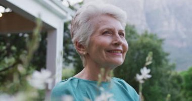 Beyaz kadın bahçesinde vakit geçiriyor. Coronavirus covid 19 salgını sırasında karantinada tek başına. Başka tarafa bakıyor ve gülümsüyor.