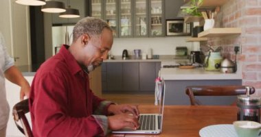 Kıdemli Afrikalı erkek ve melez ırk kadını evde vakit geçiriyorlar. Coronavirus covid 19 salgını sırasında karantinada tecrit edilmiş, kucaklıyorlar, dizüstü bilgisayar kullanıyorlar.