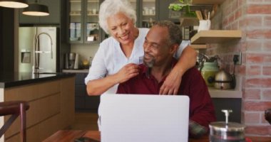 Kıdemli Afrikalı erkek ve melez ırk kadını evde vakit geçiriyorlar. Coronavirus covid 19 salgını sırasında karantinada tecrit edilmiş, kucaklıyorlar, dizüstü bilgisayar kullanıyorlar.