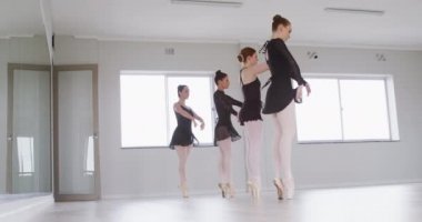 Beyaz kadın dört dansçı, siyah tricotlar giyip, yavaş çekimde, parlak bir stüdyoda, bale dersleri sırasında dans ediyorlar..