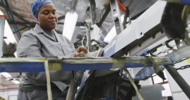 Afrikalı Amerikalı kadın araba tamircisi. Bir kasaba atölyesinde çalışıyor. Ağır çekte bir arabanın yanında öğütücü kullanıyor.