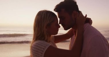 Kafkasyalı çift kumsalda vakit geçirmekten zevk alıyor, yavaş çekim günbatımında deniz kenarında alınlarına sarılıp dokunuyorlar. Rahatlatıcı Yaz Sahil Tatili.