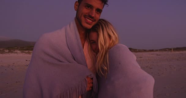 コーカシア人のカップルはビーチで時間を楽しみ ゆっくりとした動きで日没の間に毛布で身を包み カバーしています リラックスした夏のビーチ休暇 — ストック動画