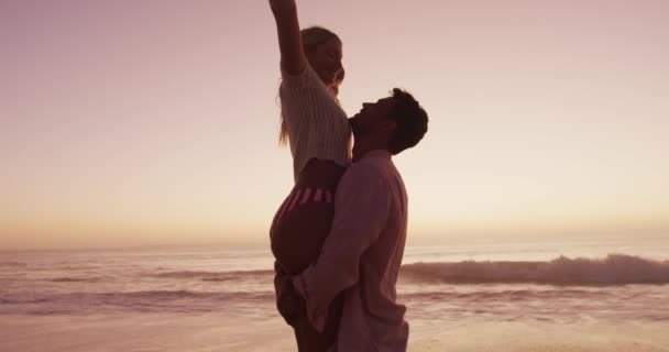 在夕阳西下的时候 一对白种人夫妇在海滩上共度时光 一个男人抱着一个女人 胳膊张开 微笑在海边 放宽暑期泳滩假期 — 图库视频影像