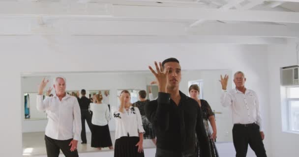 Un professeur de danse mixte prend un cours de danse de salon dans un studio de danse, démontrant des pas de danse à un groupe de personnes âgées caucasiennes au ralenti