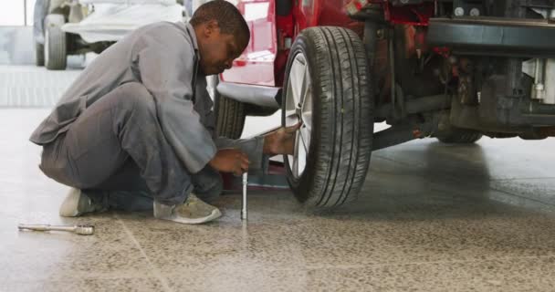 Afroamerykanin Mechanik Samochodowy Pracujący Warsztacie Miejskim Przykręcający Koło Samochodu Kluczem — Wideo stockowe